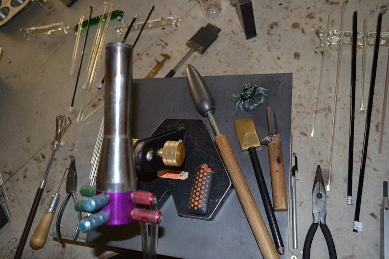 Glassworking torch, tools, and colored glass rods on the studio workbench
